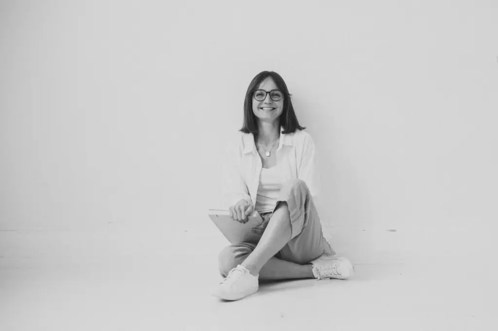 Lachende Frau (Sophie Gulich) sitzt im Schneidersitz mit Notizbuch auf dem Boden – Finanzielle Freiheit für Frauen, finanzielle Freiheit, der Weg zur finanziellen Freiheit