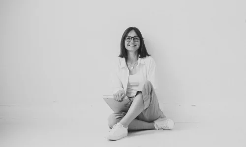 Lachende Frau (Sophie Gulich) sitzt im Schneidersitz mit Notizbuch auf dem Boden – Finanzielle Freiheit für Frauen, finanzielle Freiheit, der Weg zur finanziellen Freiheit